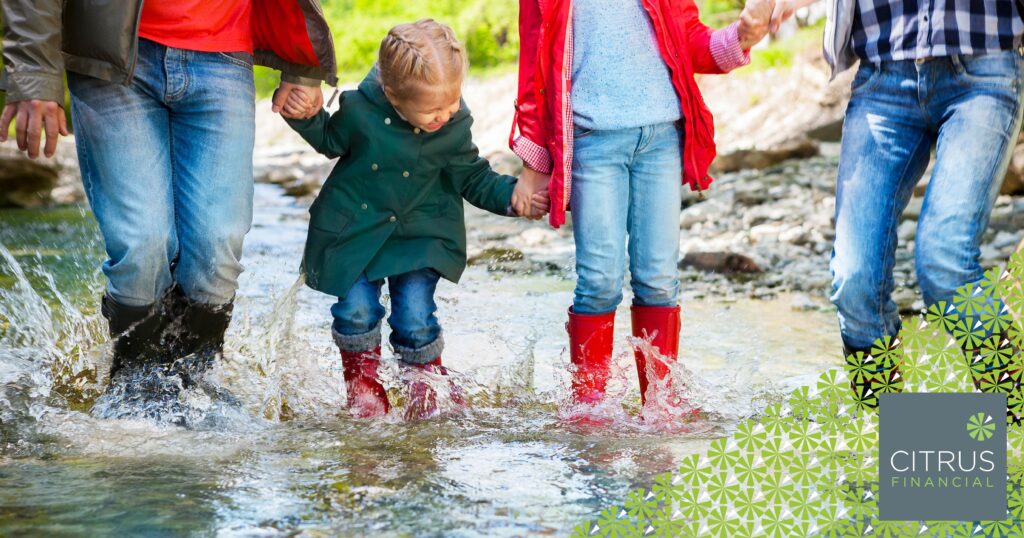 Happy family with two children wearing rain boots jumping into a mountain river