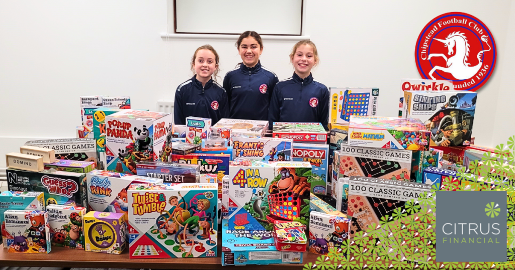 3 GIRLS WEARING cHIPSTEAD fc TRAINING TOPS STANDING BEHIND A TABLE HOLDING DONATED BOARD GAMES